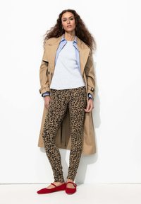Manteau beige par-dessus un haut gris, associé à des leggings à imprimé léopard et des ballerines rouges. Tissu lisse avec un design classique et un motif animal.