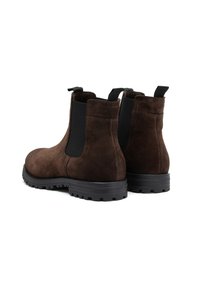 Botas Chelsea de ante marrón con paneles laterales elásticos, tiradores traseros y suela de goma negra texturizada. Forma lisa y redondeada con un detalle mínimo.