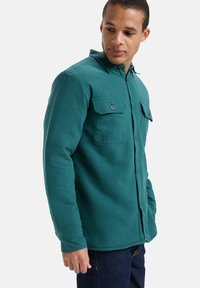 Turkusowa koszula zapinana na guziki, wykonana z miękkiego materiału, z dwoma kieszeniami na piersi, kołnierzem i długimi rękawami z prostym wykończeniem.