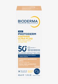 Flacon de crème solaire, blanc avec texte bleu et orange, 40 ml. L'étiquette indique SPF 50+, défense environnementale et mention "très haute protection".