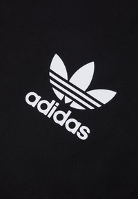 Bílá trefoil logo Adidas s třemi vodorovnými pruhy na černém texturovaném pozadí.