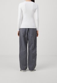 Maglietta bianca a maniche lunghe abbinata a pantaloni grigi larghi e texturizzati. I pantaloni presentano tasche e una leggera arricciatura alle caviglie.