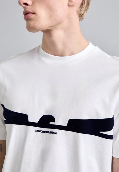 Witte katoenen t-shirt met een ronde halslijn, voorzien van een marineblauw grafisch ontwerp en het "EMPORIO ARMANI" logo dat centraal onder het ontwerp is geplaatst.