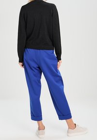 Maglione nero a maniche lunghe in tessuto strutturato, abbinato a pantaloni blu dalla vestibilità ampia con orli risvoltati, indossato con sneakers di colore chiaro.