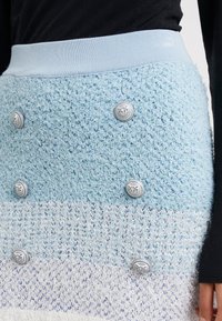 Virkat kjol med en övertoning från ljusblå till vit, med flera silverspännen och en strukturerad design. Bred elastisk midja upptill.