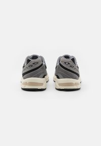 Grå sportskor med en kombination av mesh- och mockamaterial, en strukturerad sula och designaccentuerade detaljer på hälen och sidorna.