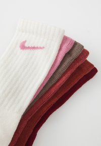 Sada piatich rebrovaných ponožiek Nike v bielej, ružovej, hnedej, vínovej a červenej farbe, s malým ružovým logom na bielej ponožke. Mäkčená pletená textúra.