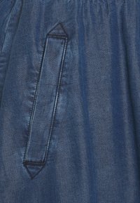 Blauer Denimstoff mit glatter Textur, ausgestattet mit einem dreieckigen aufgesetzten Taschen und einem elastischen Bund für einen sicheren Sitz.