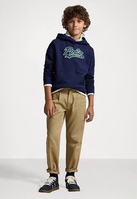 Ναυτικό hoodie με πράσινο λογότυπο "Polo Ralph Lauren", συνδυασμένο με χακί παντελόνια και ναυτικά αθλητικά παπούτσια με λευκές λεπτομέρειες. Υφασμάτινη υφή, άνετη εφαρμογή.