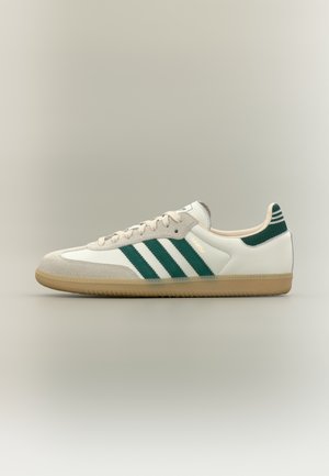 Zapatilla Adidas Samba blanca y beige con rayas verdes, suela de goma, y lengüeta trasera de punto verde con rayas blancas, vista lateral.