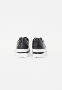 Baskets en cuir noir avec une semelle plateforme rayée blanche et noire, dotées de talons arrondis et de coutures décoratives sur les bords.