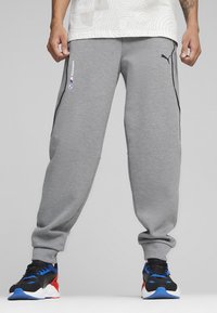 Grå sweatpants med sorte detaljer, der har sidelommer og et Puma-logo. Sammen med sorte, røde og blå træningssko.