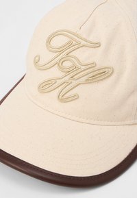Beige fabric baseball cap with brown trim on the brim and raised embroidered letters "F" and "a" in cursive on the front panel.
