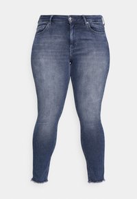 Jean skinny en denim foncé. Doté d'une taille haute, de cinq poches et d'ourlets effilochés. Le matériau présente une légère décoloration pour un effet usé.