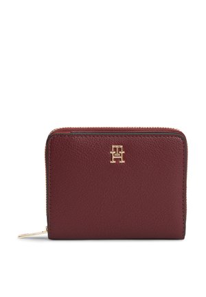 Cartera compacta de cuero rojo oscuro con cremallera dorada y pequeño logo "TH" dorado centrado en el frente.