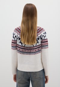 Maglione lavorato a maglia con una base crema, caratterizzato da uno scollo decorato con motivi a righe in rosso, blu navy e nero con motivi di cervi, orlo a costine e maniche lunghe.