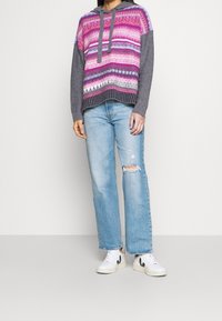 Hooded sweater in pink, purple, and gray patterns with long sleeves; paired with distressed light blue jeans and white sneakers.