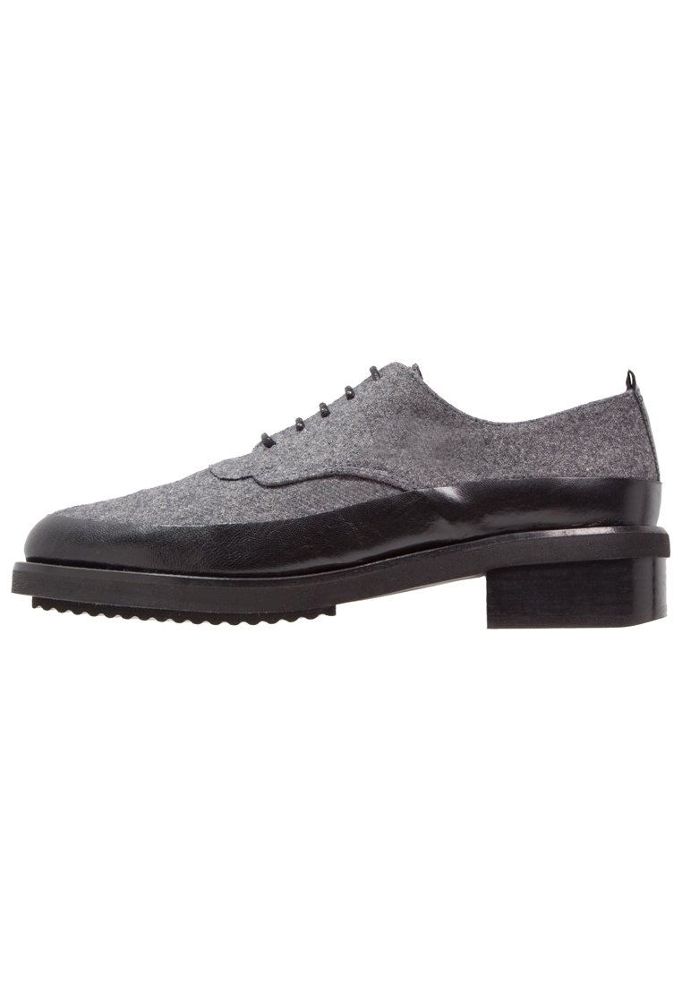 Šedá plátěná bota s černými koženými akcenty, designem wingtips, kulatými šňůrkami a blokovým podpatkem. Lehký strukturovaný svršek a gumová podrážka.