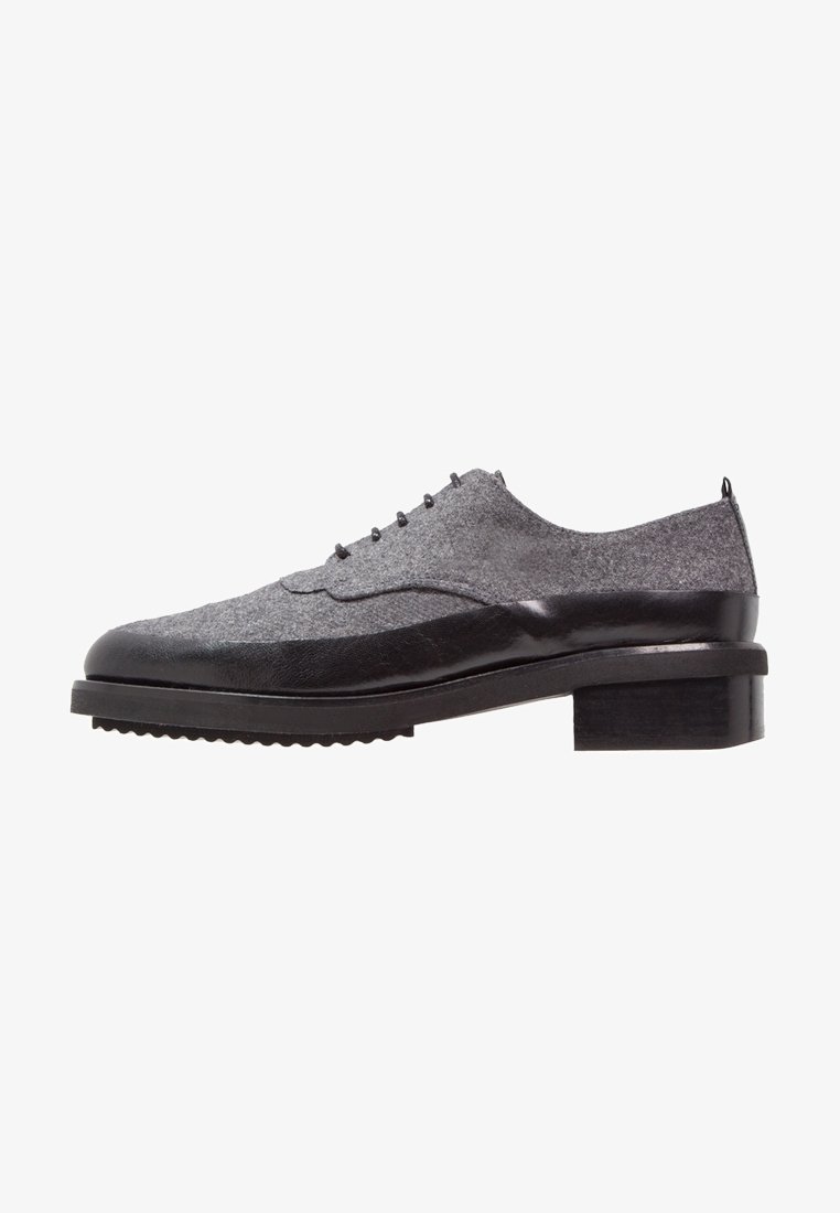 Šedá plátěná bota s černými koženými akcenty, designem wingtips, kulatými šňůrkami a blokovým podpatkem. Lehký strukturovaný svršek a gumová podrážka.