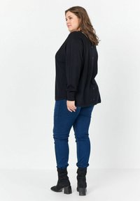 Top nero a maniche lunghe con una vestibilità rilassata, caratterizzato da un orlo dritto e dettaglio con bottoni sul retro. Abbinato a jeans blu aderenti e stivaletti neri.