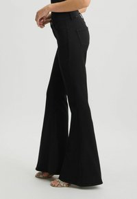 Pantaloni flared neri con vita alta, realizzati in un tessuto liscio. Dotati di tasche e chiusura con bottone, presentano una leggera lucentezza e una silhouette dritta.