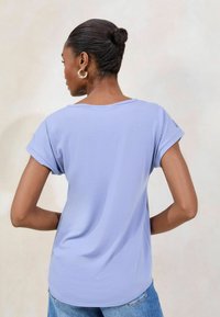 Tricou violet deschis cu un croi lejer, mâneci pliate și guler rotund. Textură netedă cu un luciu subtil. Design minimalist.