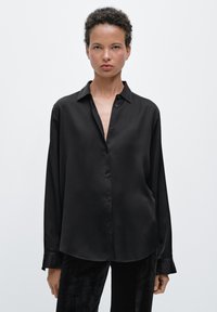 Button-up black satin shirt with a collar, featuring a loose design, long sleeves, and a smooth texture.