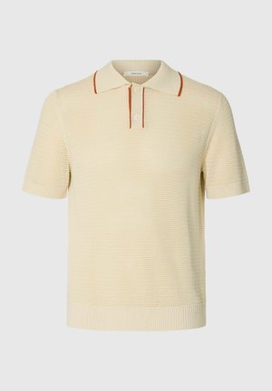 Polo en maille manches courtes couleur crème avec tissu texturé, patte à deux boutons et fines rayures couleur rouille sur les bords du col et de la patte.