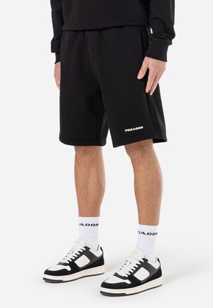 Zwarte katoenen shorts met een elastische tailleband, met het "PEGADOR"-logo in het wit. Gecombineerd met zwart-witte sneakers en witte sokken.