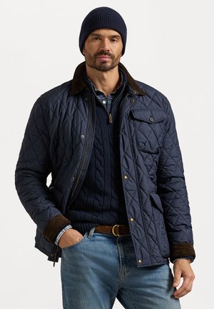 Marineblaue gesteppte Jacke mit braunem Cordkragen, Reißverschluss und Druckknopfverschluss sowie seitlichen Taschen. Trägt man über einem marineblauen grob gestrickten Pullover und einem karierten Hemd.