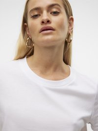 Hvit bomulls t-skjorte med rund hals. Modellen har på seg store gullringøredobber. Glatt tekstur, minimalistisk design. Mykt lys.
