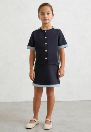 Tmavomodré šaty s krátkymi rukávmi, svetlomodrými akcentmi a striebornými gombíkmi. Majú priliehavý strih a jednoduchý, na mieru šitý tvar.
