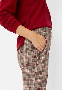 Rode gebreide trui gecombineerd met bruine geruite broek met hoge taille, voorzien van zijzakken en een gestructureerd, geweven stofpatroon.