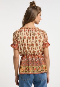 Blusa floreale con maniche corte a volant, colletto elastico, con motivi beige, rossi e verdi, abbinata a jeans in denim blu.