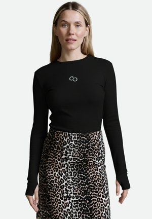 Schwarzes Langarmoberteil mit gerippter Textur und einem Unendlichkeitssymbol-Design. Kombiniert mit einem Rock im Leopardenmuster in Beige und Schwarz.