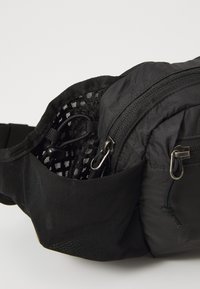 Schwarze Nylon-Hüfttasche mit mehreren Fächern, ausgestattet mit einer Netz-Tasche und Reißverschlussfächern. Strukturierte Oberfläche und verstellbarer Gurt sind enthalten.