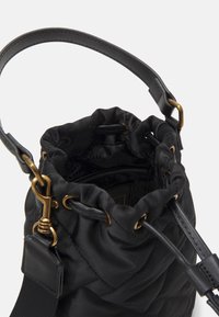 Černá prošívaná látková taška ve tvaru kbelíku s utahovací šňůrkou, hladkými koženými detaily a zlatými kovovými prvky. Uvnitř se nachází vzorované podšívka.