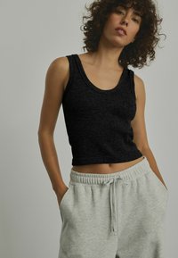 Top in cotone nero a coste con scollo rotondo, abbinato a pantaloni della tuta grigi chiari con vita elastica. Il top presenta una vestibilità corta e un tessuto testurizzato.