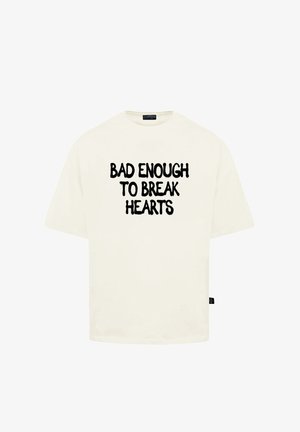 Krémové tričko s krátkým rukávem a volným střihem, na přední i zadní straně s tučným černým textem "DOST ŠPATNÉ NA TO, ABY SE ZLOMILO SRDCE".