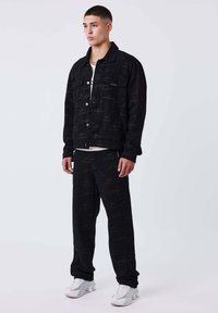 Conjunto de chaqueta y pantalones de mezclilla negra con un sutil patrón geométrico. La chaqueta tiene cierre de botones y dos bolsillos delanteros.