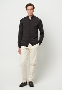 Suéter de cremallera gris oscuro con cuello alto, combinado con pantalones color crema y zapatos oscuros. Textura suave, diseño ajustado, acentos mínimos.