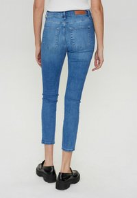 Tievie zils denim bikses ar vidēju vidukli, piecām kabatām un rupjiem piedurkņu galiem. Aizmugures vidukļa daļā atrodas brūnas ādas plāksne.