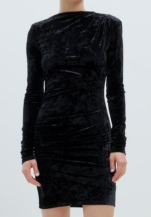 Schwarzes Samtkleid mit langen Ärmeln, das eine taillierte Silhouette, geraffte Seitendetails und einen runden Ausschnitt aufweist, wodurch eine glatte, weiche Textur entsteht.