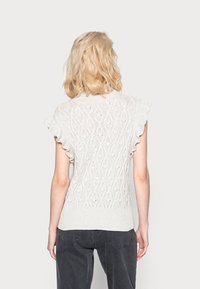 Pull en maille gris clair avec manches courtes à volants, présentant un motif décoratif en losanges et une finition texturée.