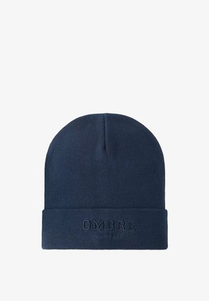 Gorro de punto azul marino con un dobladillo que presenta el texto en relieve "OMBRE" y "SINCE 1965" en un tono más oscuro. Textura suave.