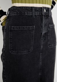 Jupe en denim noir taille haute à la silhouette droite, avec deux poches arrière et un dégradé subtil, détails cousus autour de la taille.