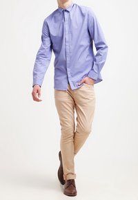 Jasnoniebieska koszula zapinana na guziki, z długimi rękawami, w zestawieniu z beżowymi chinosami i brązowymi butami. Gładka tkanina z klasycznym kołnierzem. Luźny krój.