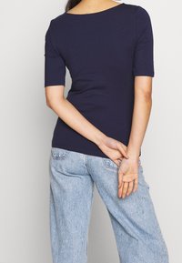 Dunkelblaues, eng anliegendes T-Shirt mit rundem Halsausschnitt und kurzen Ärmeln, kombiniert mit hellblauen, hochgeschnittenen Jeans aus Denim mit einer leicht ausgewaschenen Textur.