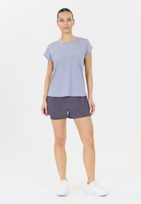 Ljusblå randig kortärmad topp i kombination med mörkgrå sportshorts. Modellen bär vita sneakers. Ren bakgrund, neutrala färger.