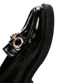 Schwarze Lacklederslipper mit runder Zehenform, ausgestattet mit einem goldenen, runden Hardware-Akzent und einer strukturierten Gummisohle.